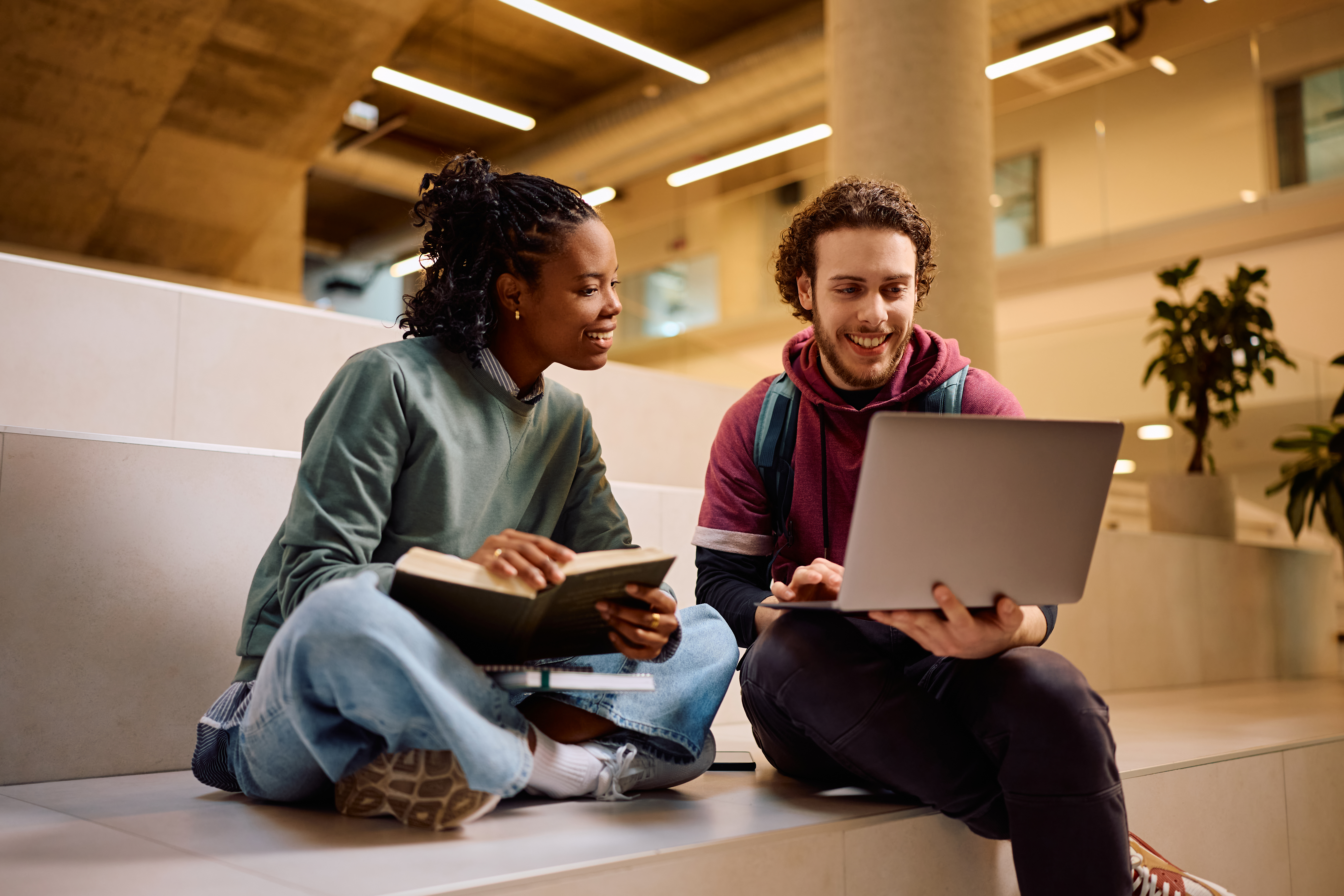 Happy student and his African American female friend using laptop while learning together at the university.