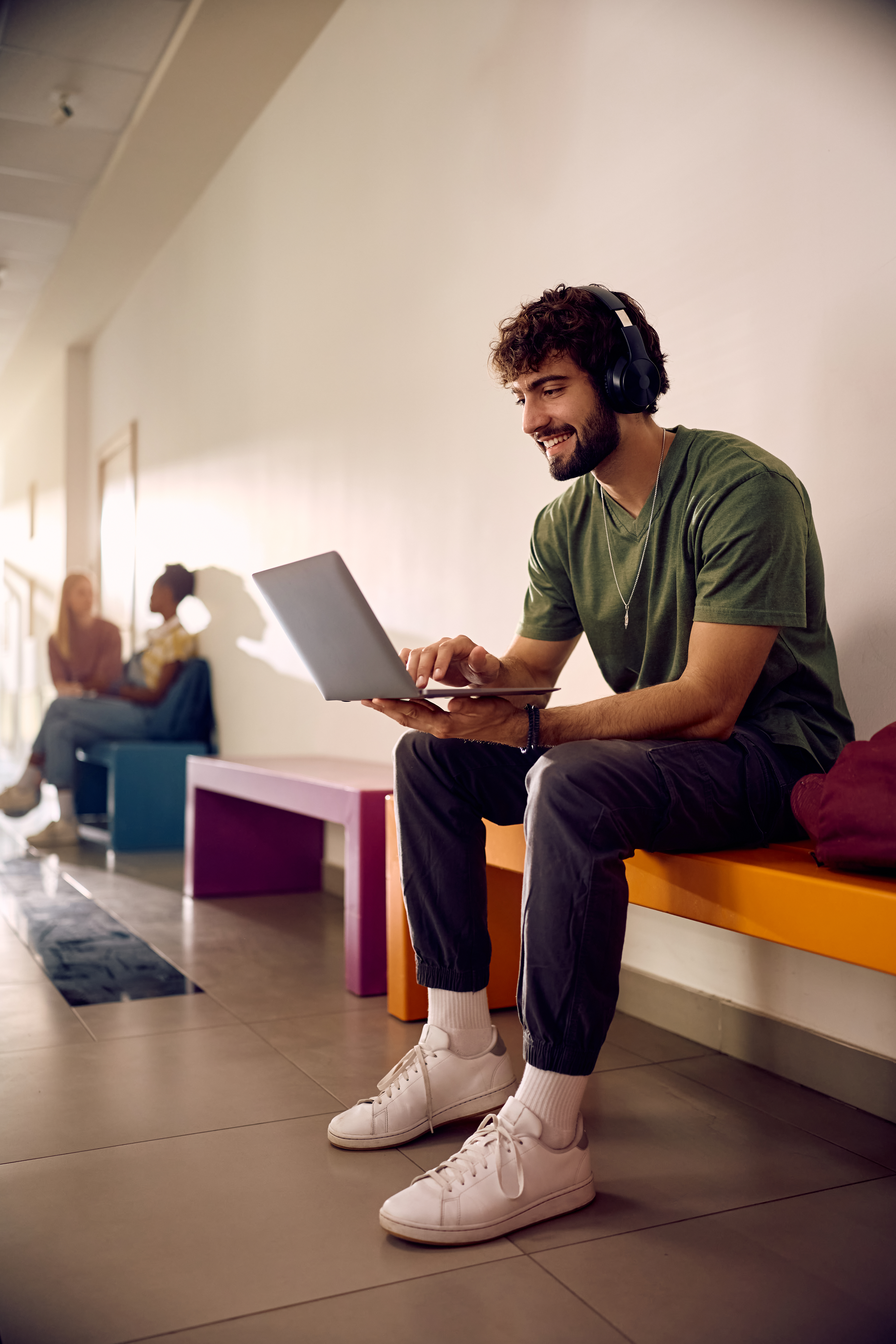 Happy student surfing the net on laptop at university hallway.
